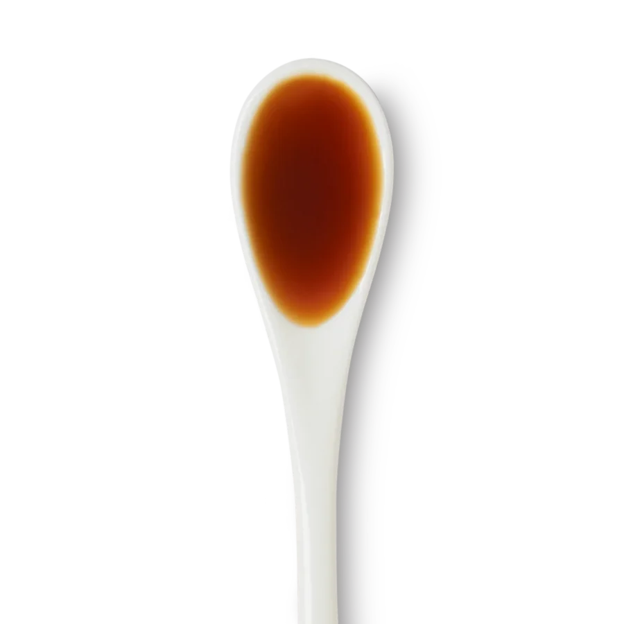 A white ceramic spoon filled with a small amount of dark brown liquid, viewed from above on a white background.