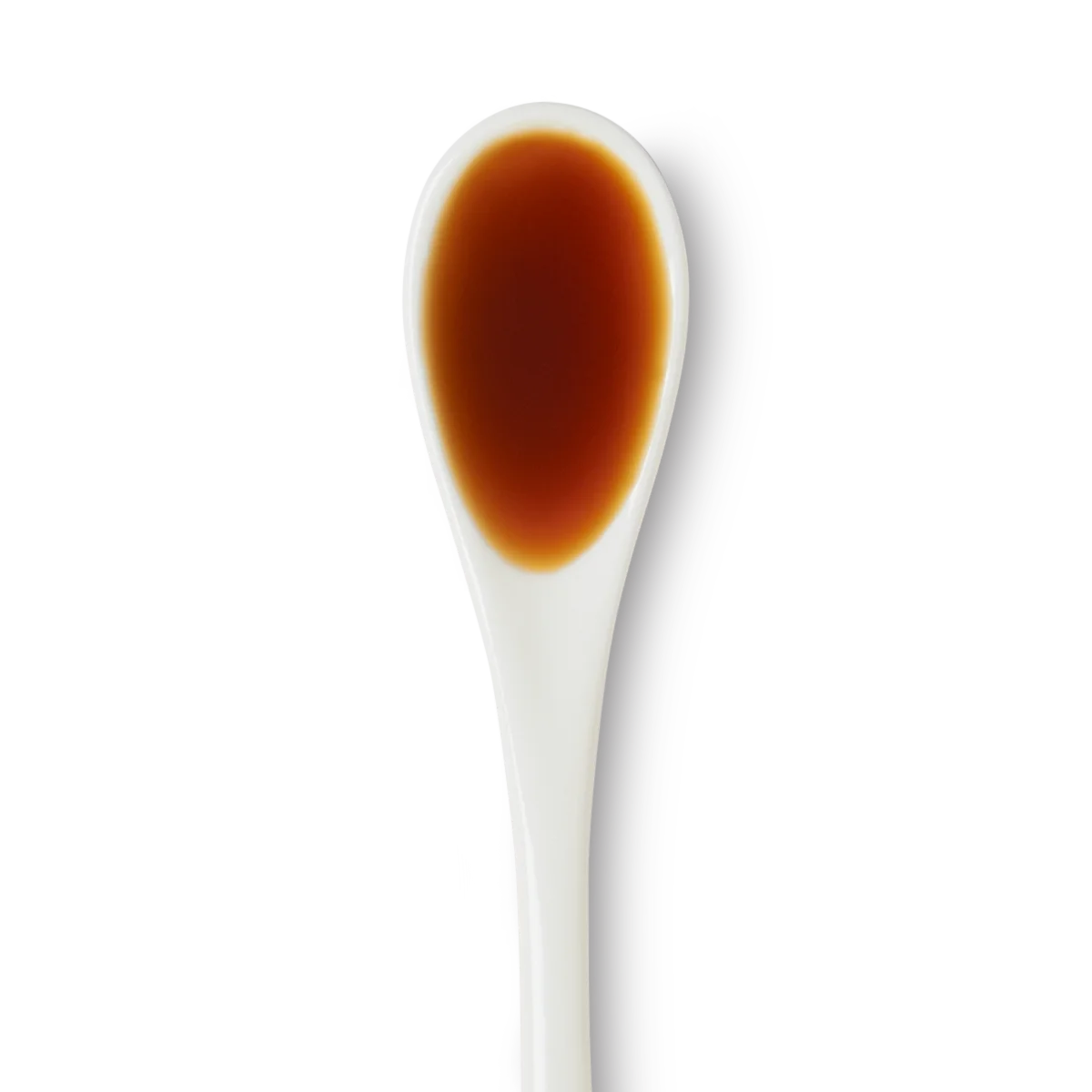 A white ceramic spoon filled with a small amount of dark brown liquid, viewed from above on a white background.