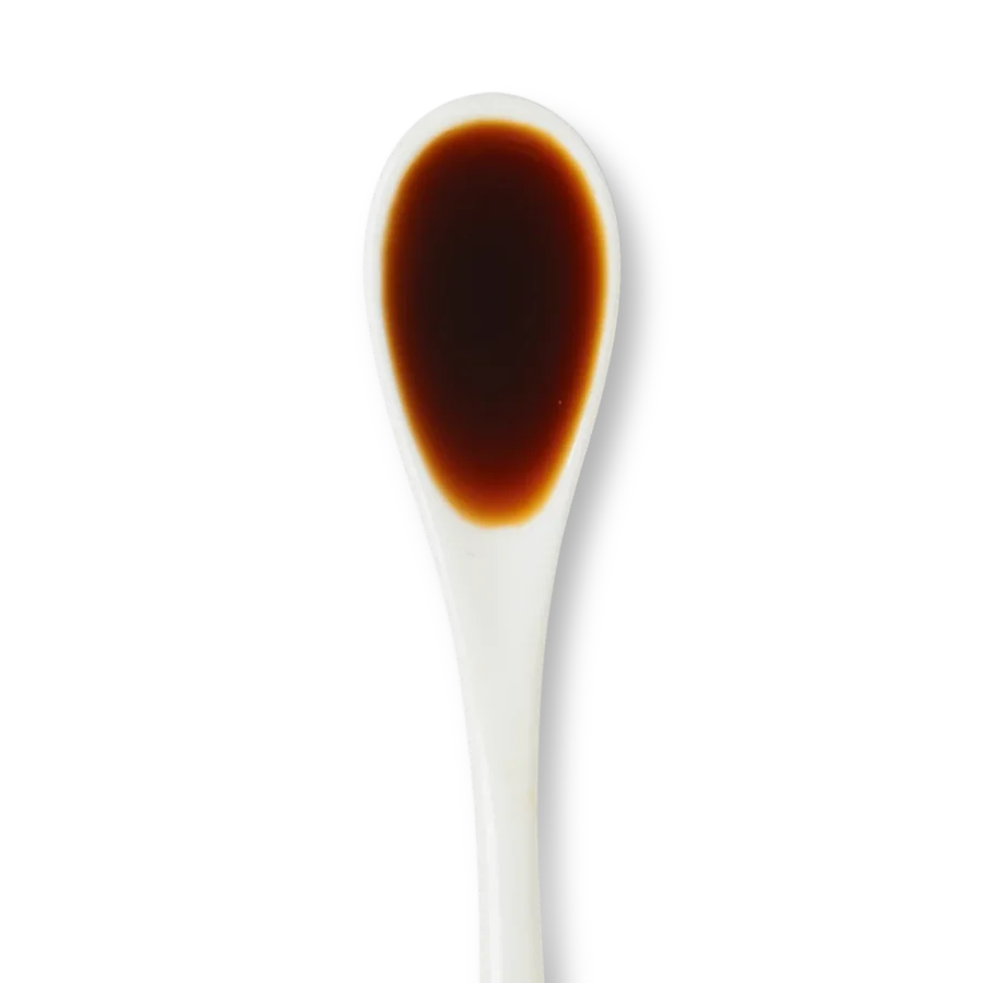A white ceramic spoon filled with a small amount of dark brown liquid, likely soy sauce, against a white background.
