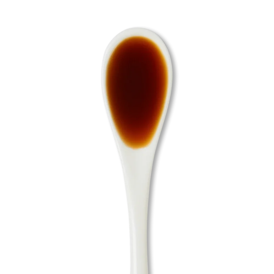 A white ceramic spoon filled with dark brown liquid, possibly soy sauce, against a white background.