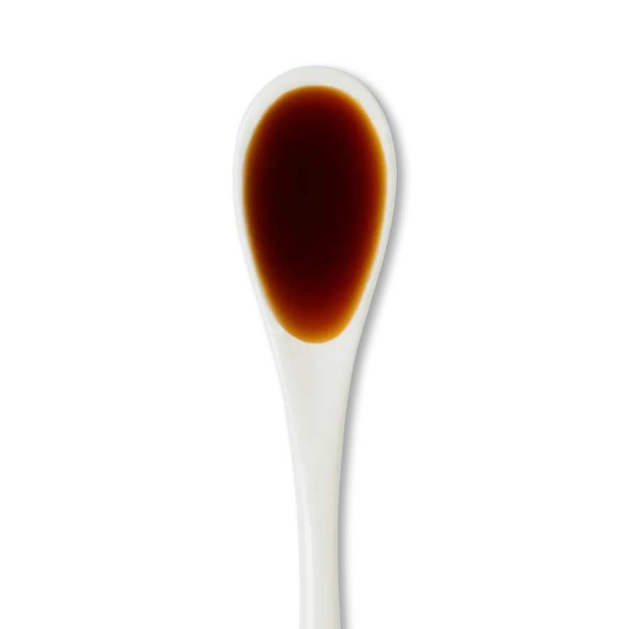A white ceramic spoon filled with dark brown liquid, likely soy sauce, against a plain white background.