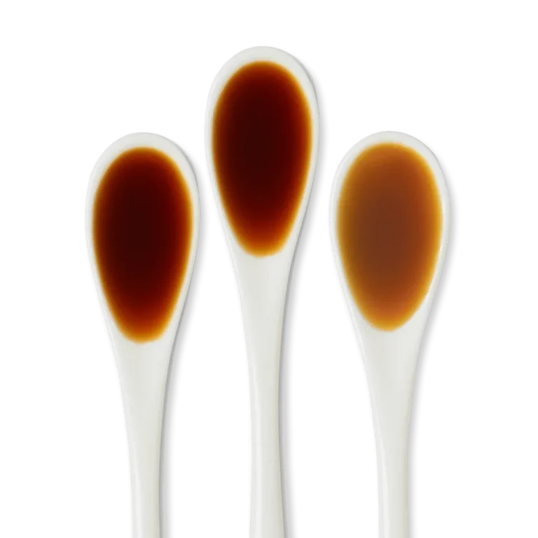 Three clear spoons each containing a different shade of brown liquid, displayed on a white background.