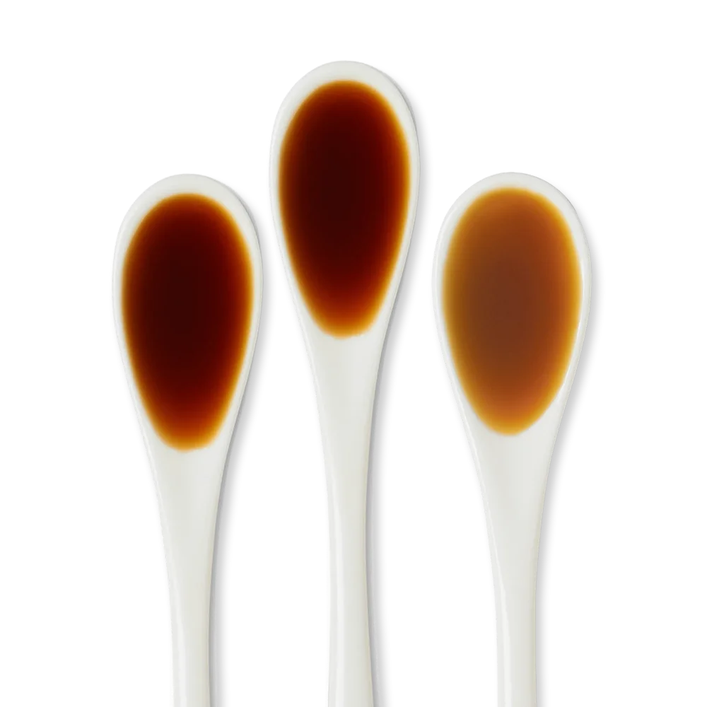 Three clear spoons each containing a different shade of brown liquid, displayed on a white background.