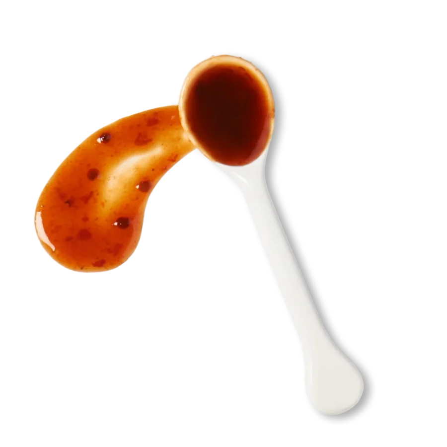 A white spoon with a reddish-brown sauce, with some sauce spilled next to the spoon on a white background.