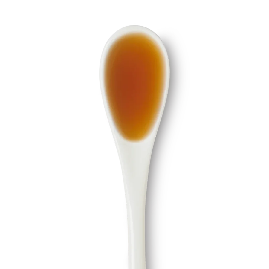 A white ceramic spoon filled with brown liquid, photographed against a white background.