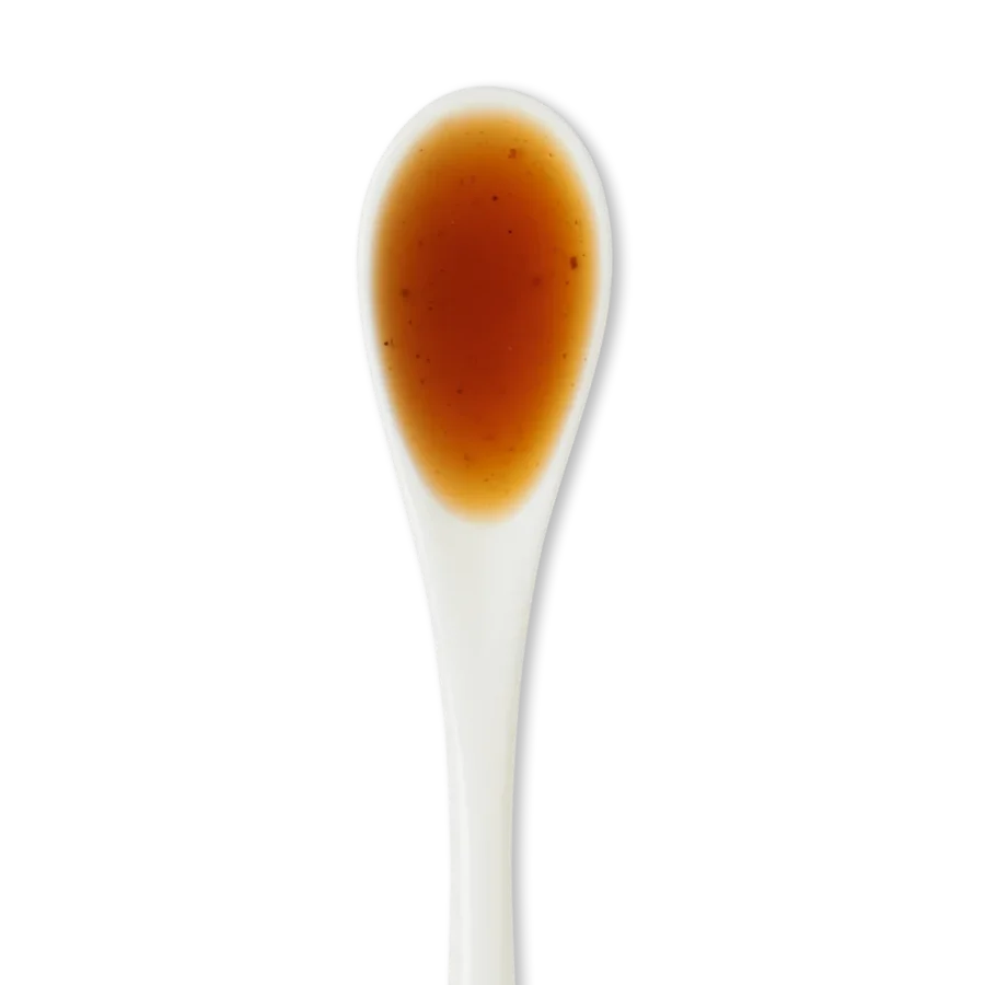 A white ceramic spoon filled with brown liquid against a white background.