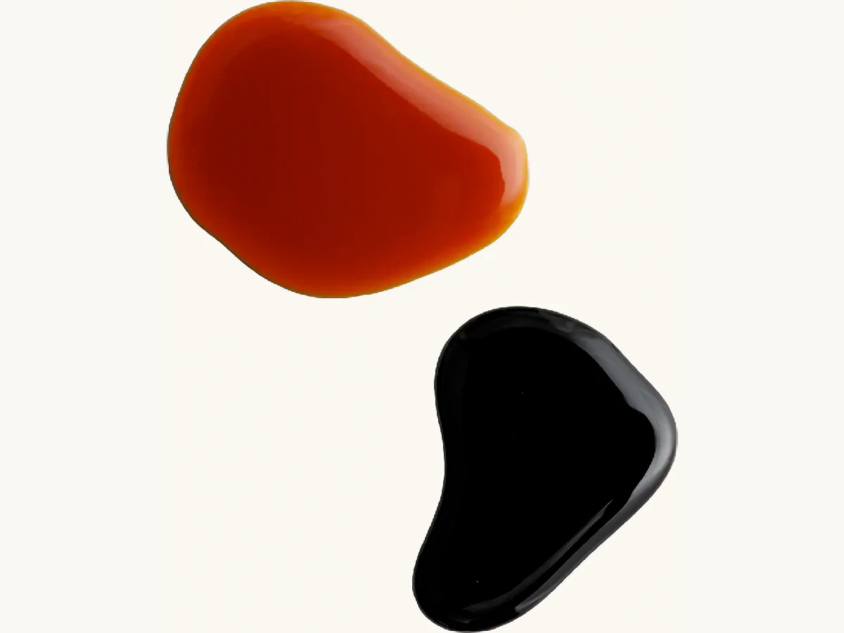 Two irregularly shaped blobs of liquid, one red and one black, on a white background.