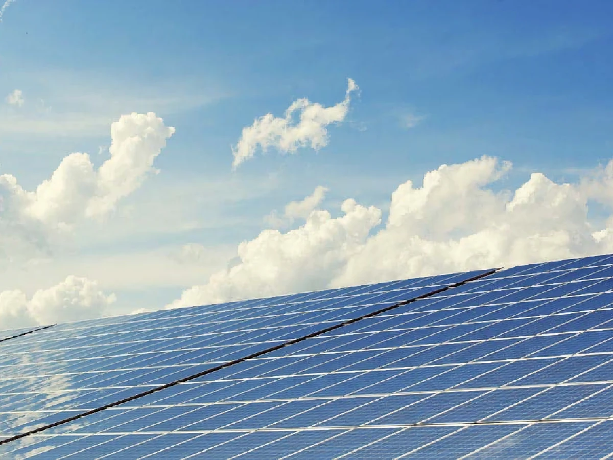Rows of solar panels under a blue sky with scattered clouds.
