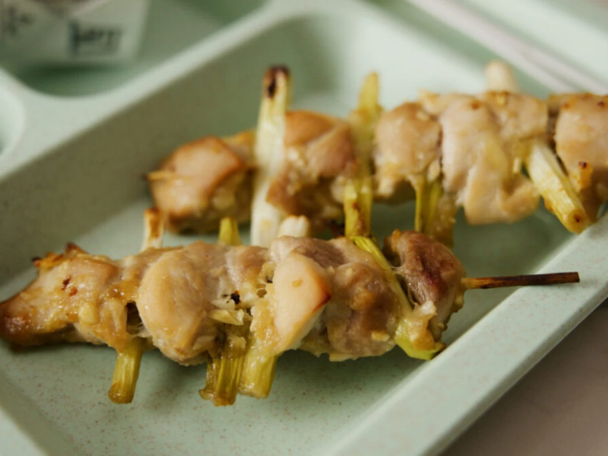 Two wooden skewers with grilled chicken pieces and green vegetables served on a light green tray.