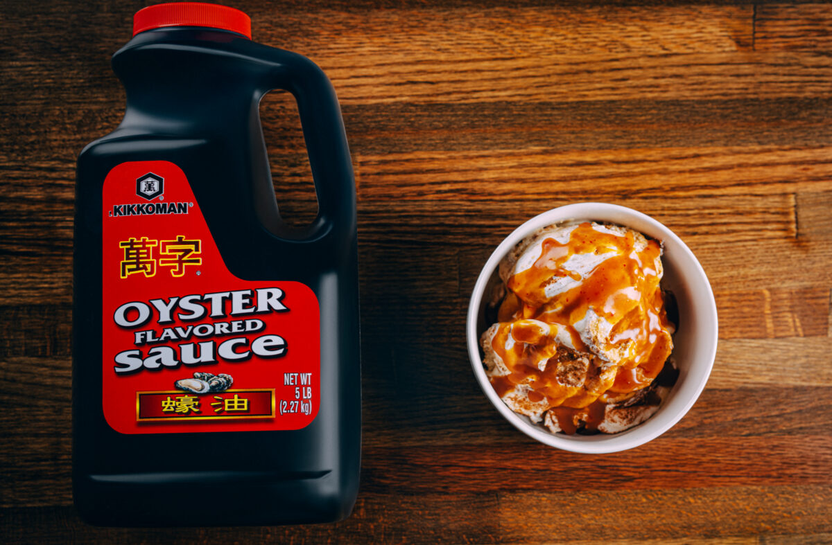 A layered banana pudding topped with whipped cream and drizzled with glossy gochujang caramel sauce, featuring Kikkoman® Soymilk and Kikkoman® Oyster Sauce for rich, savory-sweet flavor.