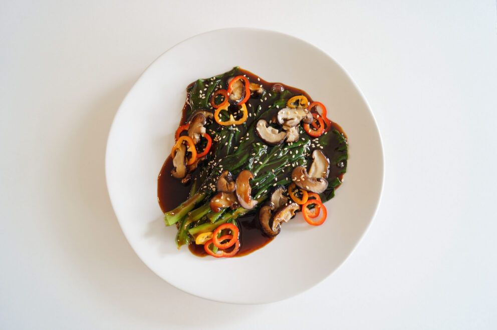 Stir-fried gai lan and shiitake mushrooms coated in a glossy Kikkoman hoisin-mirin glaze, topped with sesame seeds and sliced peppers.