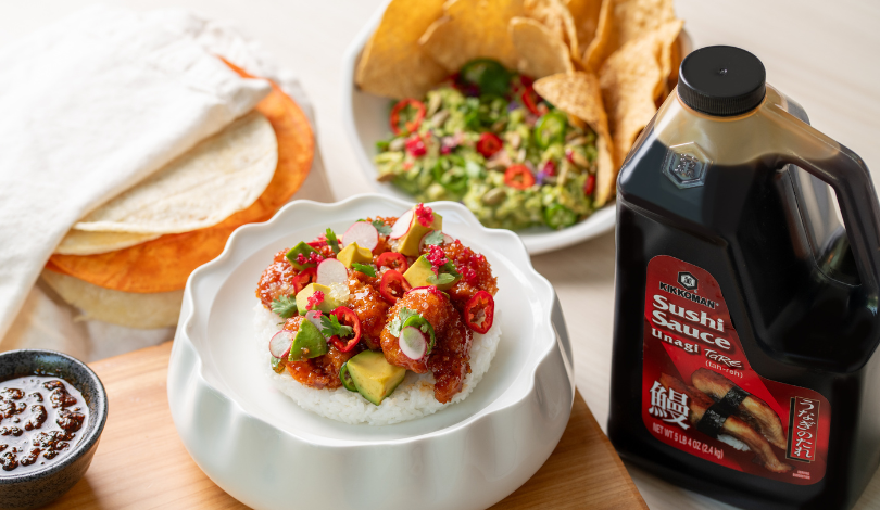 A bowl of rice topped with sauced fish, avocado, and herbs is shown beside sushi sauce, guacamole with chips, flatbreads, and a small dish of sauce on a table.