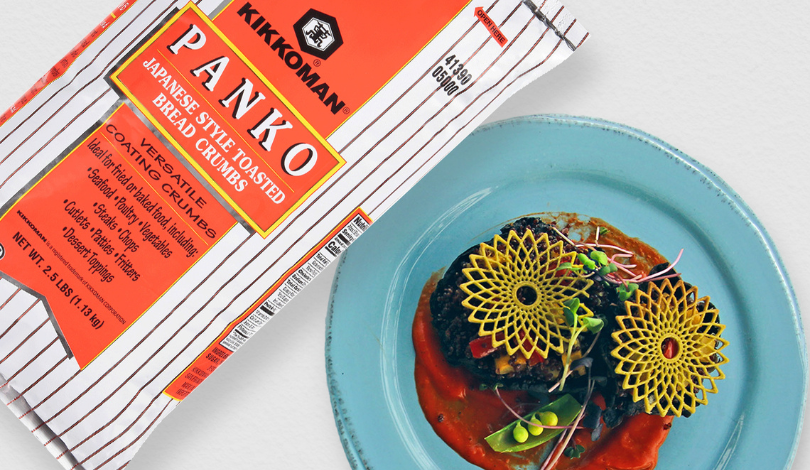 A bag of Kikkoman panko bread crumbs sits next to a blue plate with two decorated patties on red sauce, garnished with yellow crisps and microgreens.
