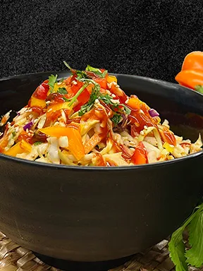 A black bowl filled with a colorful vegetable salad, topped with chopped herbs and a drizzle of red sauce, set against a dark background.