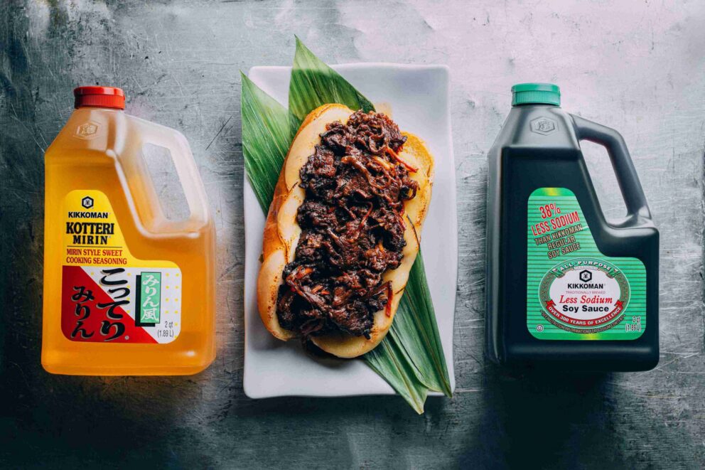 A dish topped with braised meat is placed on a leaf between bottles of Kikkoman Kotteri Mirin on the left and Kikkoman soy sauce on the right.