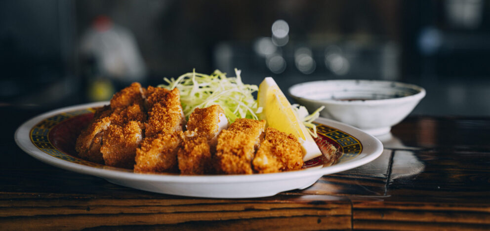 A plate of breaded, fried meat cutlets served with shredded cabbage and a lemon wedge, with a small bowl of sauce in the background.