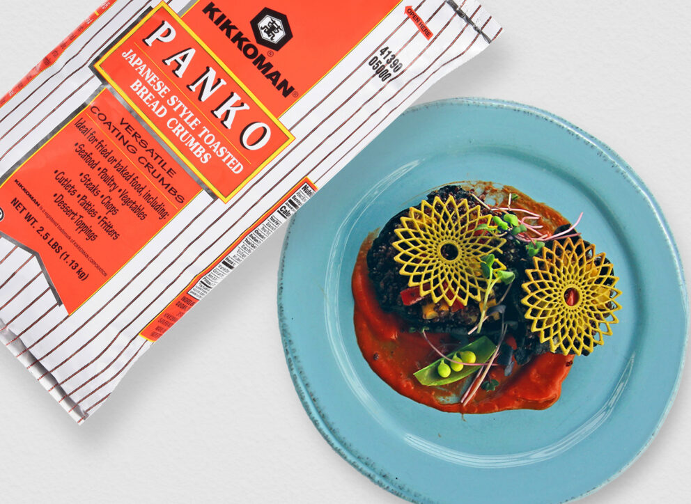 A bag of Kikkoman Panko bread crumbs is tilted over a blue plate with a gourmet dish garnished with sauce, microgreens, and yellow decorative crisps.