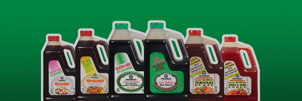 A row of seven large Kikkoman sauce bottles, including soy sauce, teriyaki, sweet and sour, teriyaki glaze, and gluten-free varieties, against a green background.
