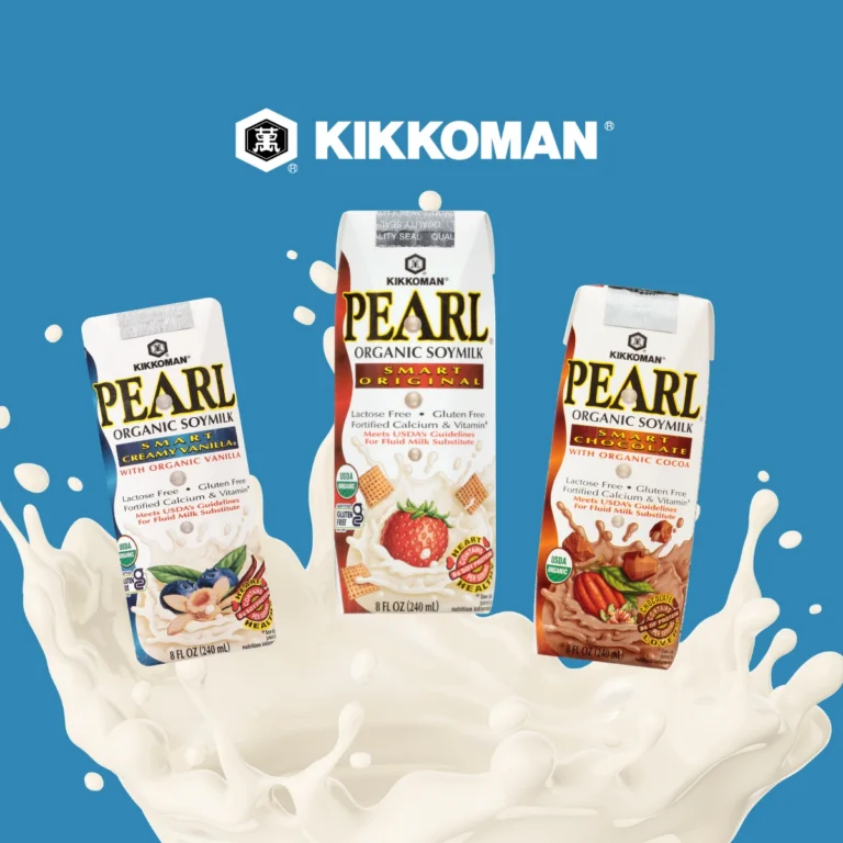 Three Kikkoman Pearl Organic Soymilk cartons—vanilla, original, and cocoa—stand above a splash of soymilk on a blue background with the Kikkoman logo above them.