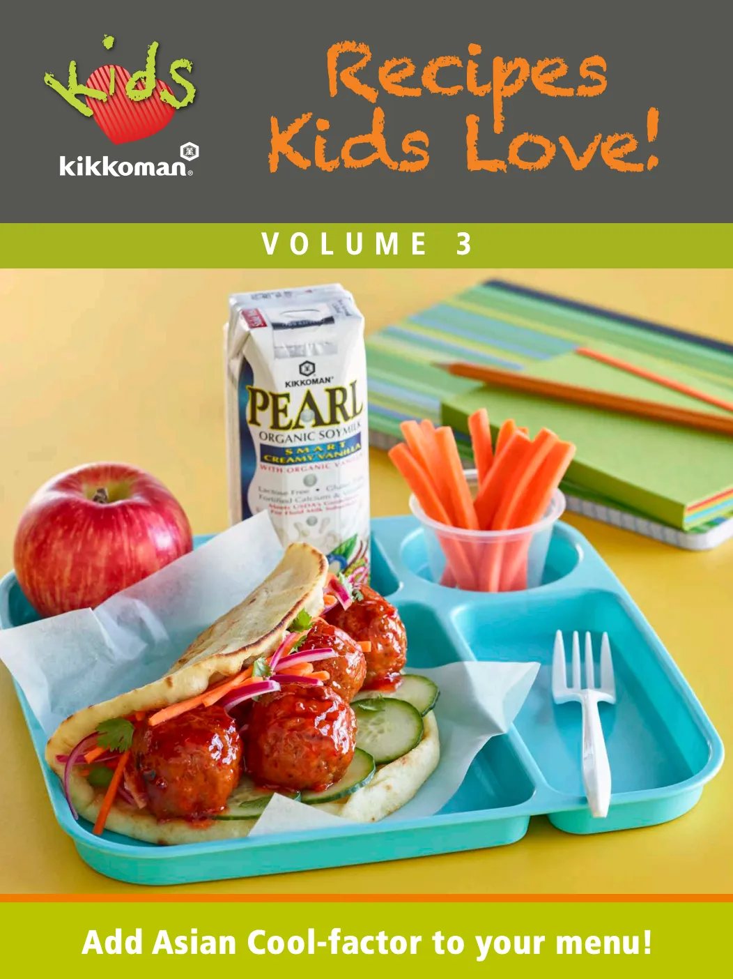 A school lunch tray with a wrap, meatballs, cucumber slices, an apple, carrot sticks, and a carton of organic soy milk. A cookbook titled "Recipes Kids Love! Volume 3" is shown.