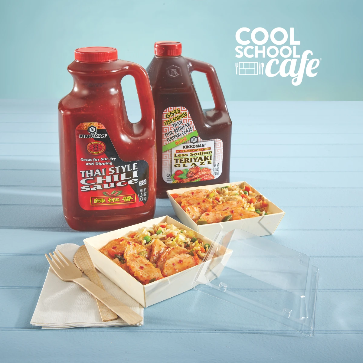 Two large bottles of Thai-style chili sauce and teriyaki sauce behind two trays of prepared Asian-style noodle dishes, with napkins and utensils on the side. "Cool School Cafe" logo in corner.
