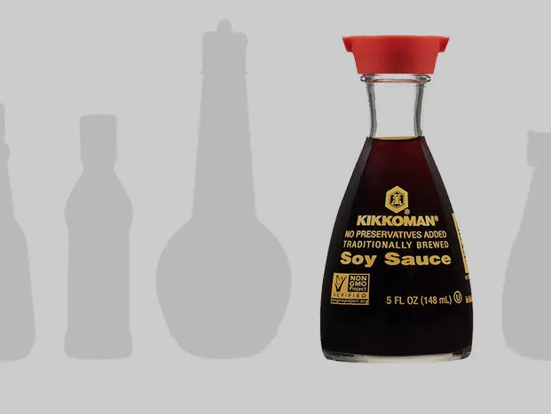 A bottle of Kikkoman soy sauce with a red cap is displayed on a grey background with outlines of bottles in the background.