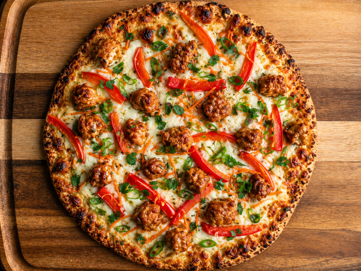 A baked pizza topped with sausage, red bell pepper strips, chopped green herbs, and melted cheese on a wooden board.