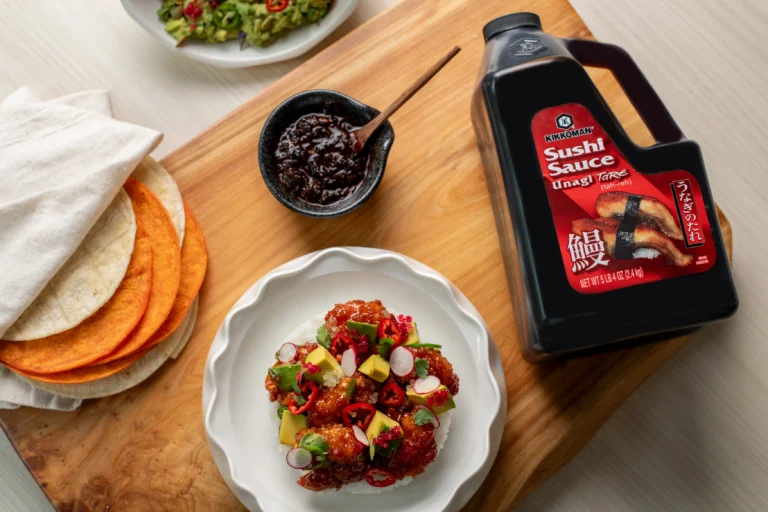 A wooden board with a jug of Kikkoman Sushi Sauce, a bowl of diced vegetables and meat, tortillas, and a small bowl of dark sauce.