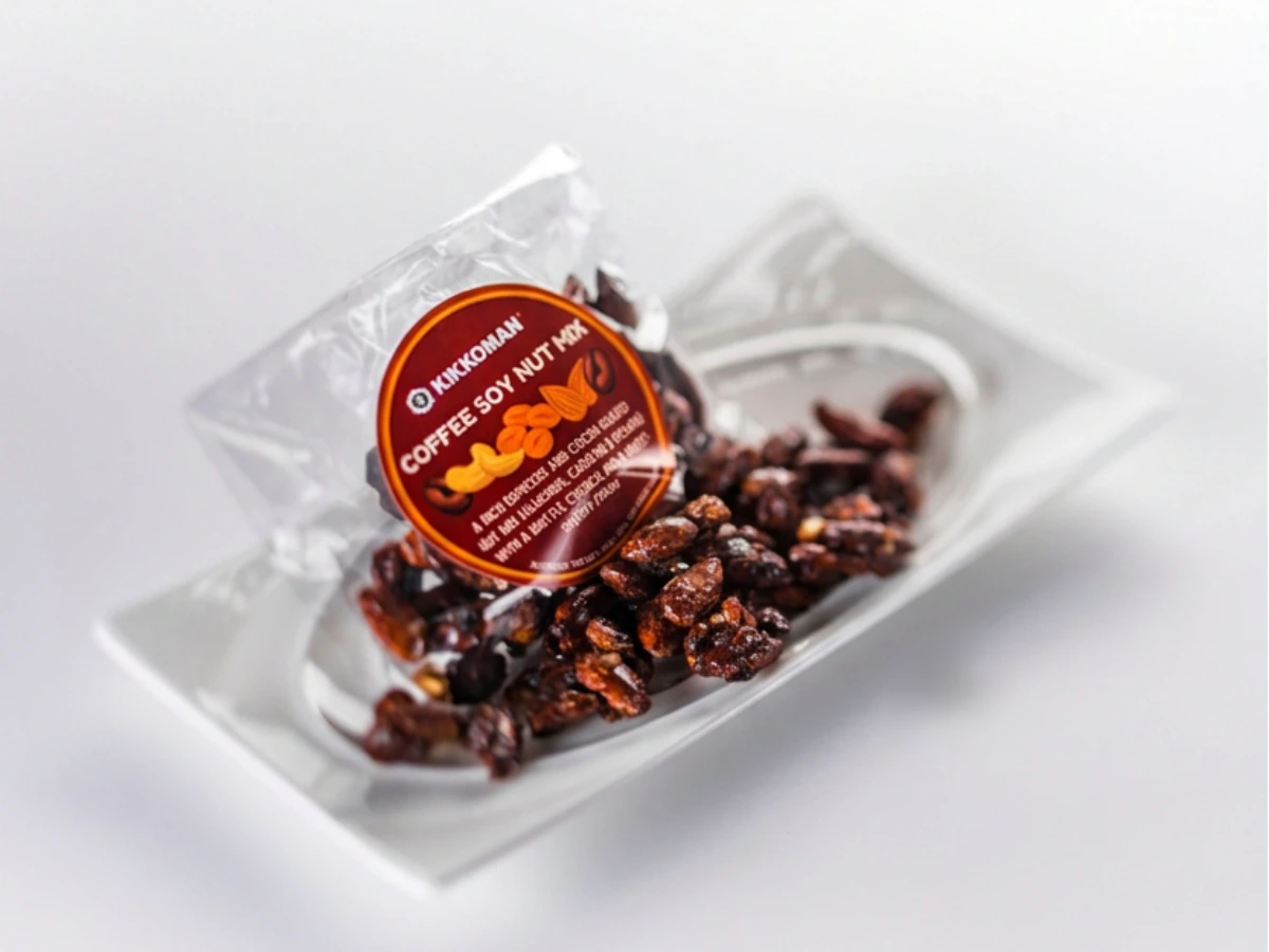A packet labeled “Coffee Soy Nut Mix” sits open on a metal tray, with roasted nuts and beans scattered in front of the packaging.