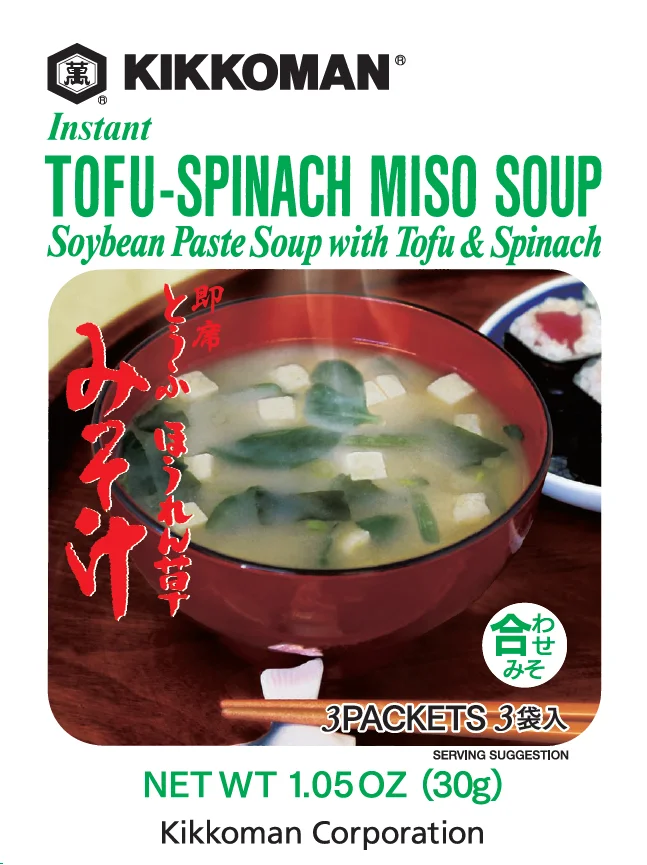 A bowl of tofu-spinach miso soup with tofu cubes and spinach leaves, chopsticks, and a soup spoon, featured on Kikkoman Instant Tofu-Spinach Miso Soup packaging.