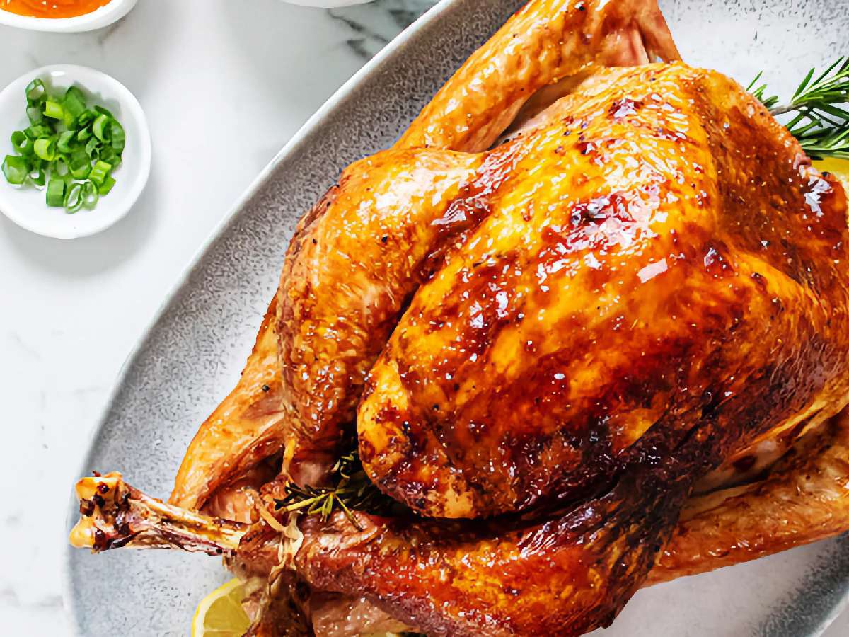 Roast turkey with golden-brown skin served on a platter, garnished with herbs and lemon; small bowls of condiments are visible nearby.