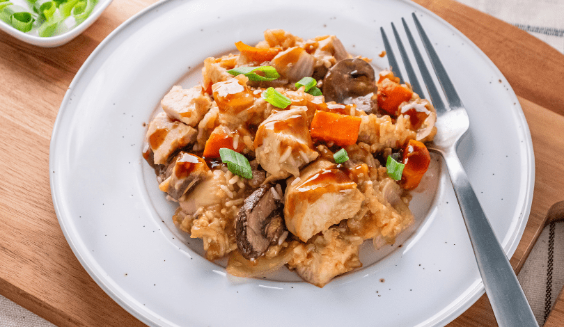 A plate of tofu and vegetable stir-fry with mushrooms, carrots, and green onions, served with rice and drizzled with sauce. A fork rests on the plate.