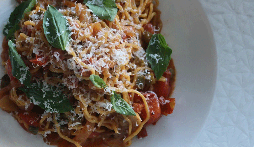 A bowl of pasta topped with tomato sauce, grated cheese, and fresh basil leaves, served on a white plate.