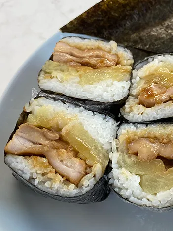Four pieces of sushi wrapped in seaweed, filled with chicken, rice, and cooked vegetables, are arranged on a white plate.