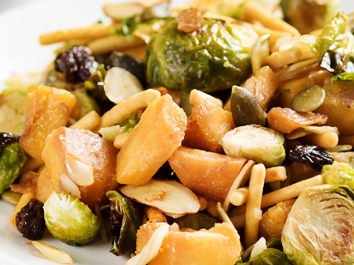 A plate of roasted Brussels sprouts, diced roasted sweet potatoes, sliced almonds, pumpkin seeds, dried cranberries, and crunchy chow mein noodles.