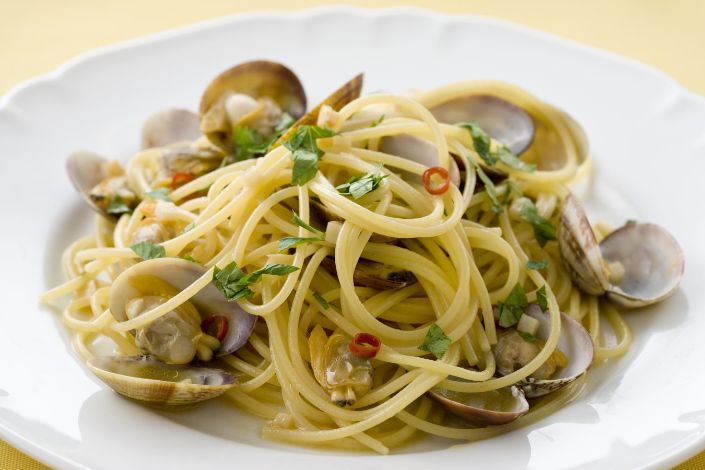 A plate of spaghetti with clams, garnished with chopped parsley and red chili slices, served on a white dish.