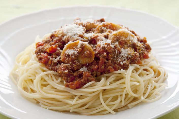 A plate of cooked spaghetti topped with meat and tomato sauce, mushrooms, and grated cheese, served on a white dish.