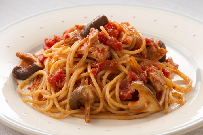 A plate of spaghetti topped with tomato sauce, mushrooms, and pieces of meat on a white dish.