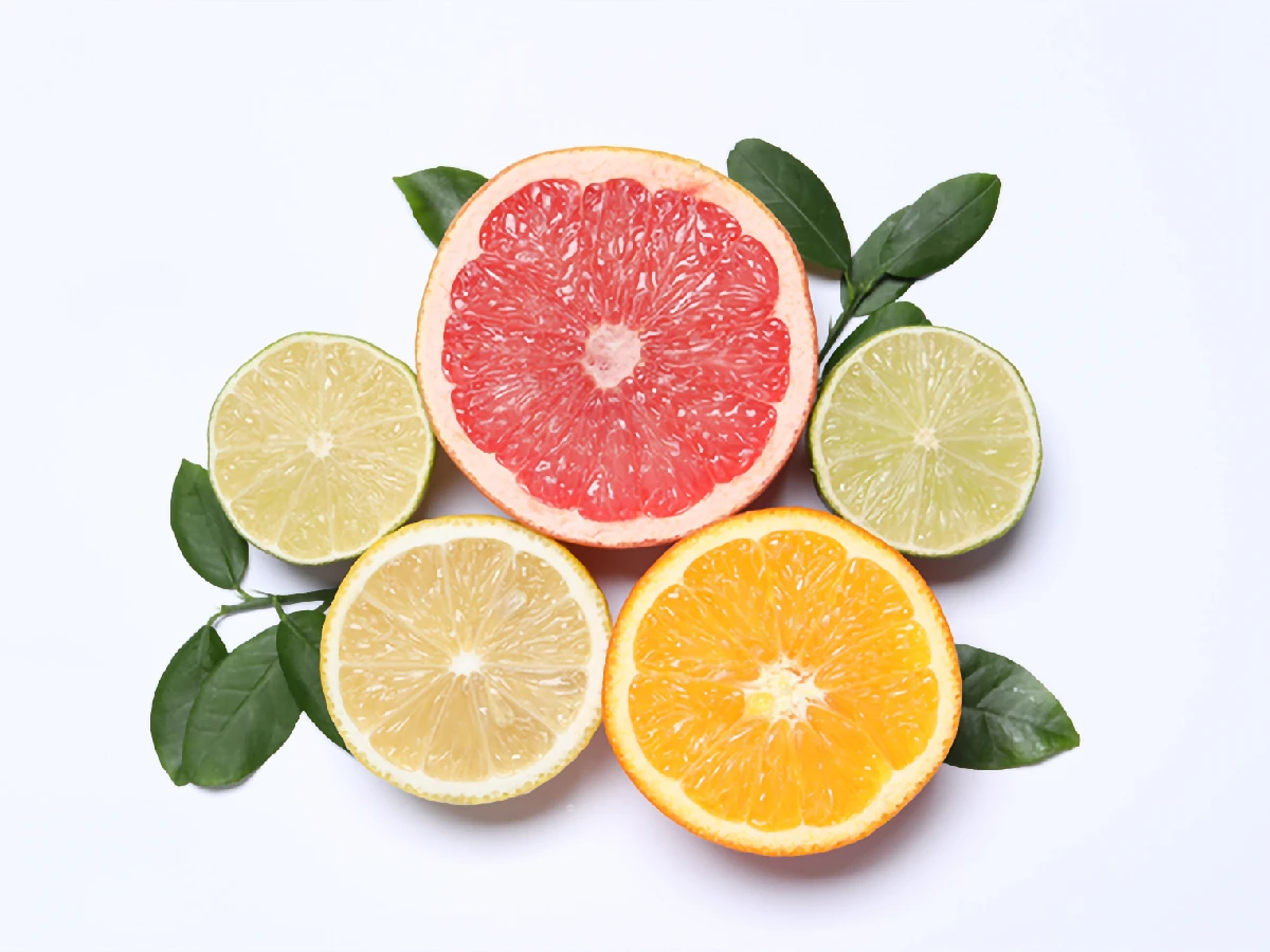 A halved grapefruit, orange, lemon, and two limes are arranged on a white background with green leaves.
