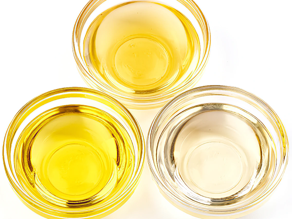 Three small glass bowls filled with different types of cooking oil, each with a distinct shade of yellow and clear, arranged on a white surface.