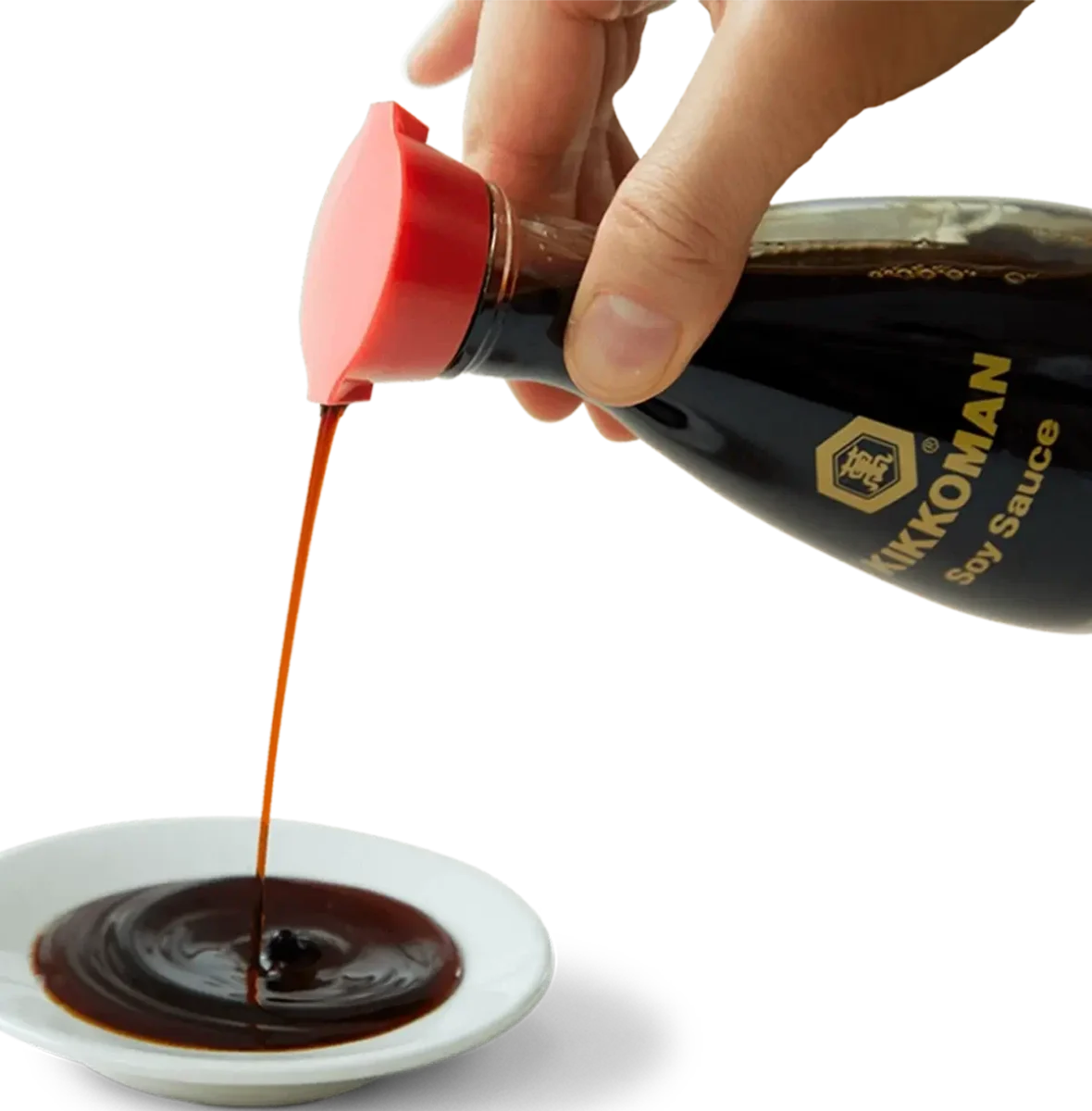 A hand pours Kikkoman soy sauce from a bottle with a red cap into a small white dish.