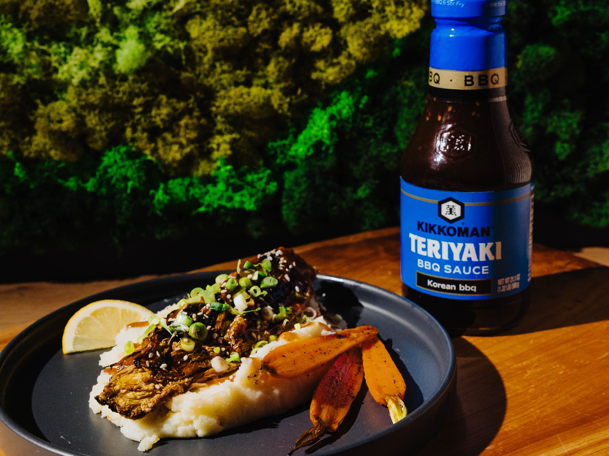 Grilled fish on mashed potatoes with carrots and green onions, served with a lemon wedge. Kikkoman Teriyaki BBQ Sauce bottle in the background.