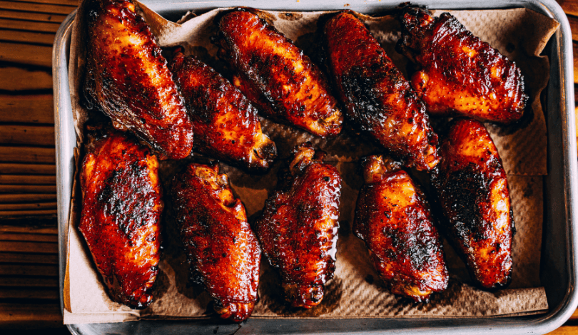 A baking tray lined with brown paper holds ten cooked, glazed chicken wings arranged in two rows.