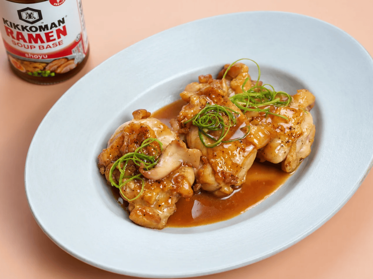 Chicken pieces covered in brown sauce, garnished with sliced green onions, served on a white plate; a bottle of Kikkoman ramen soup base is visible in the background.